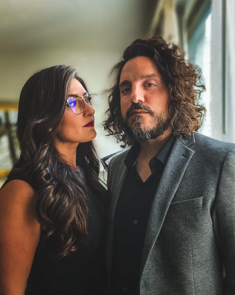 Mike and Zoja Falzone dressed up in front of a window, Zoja gazing at Mike while he looks at the camera